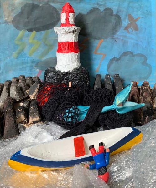 a photo of a junk art model with a dolphin caught in a net, a fisherman falling out of his boat and the lighthouse in the background.