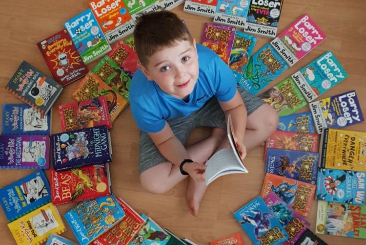 Josh Cullen, a pupil at Hollybush Primary School in Derry sitting on the floor surrounded by books