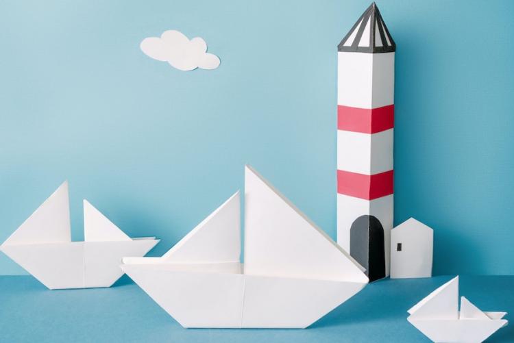 Origami boats sail in front of a cardboard lighthouse